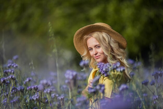 Loira jovem e bonita com um chapéu percorre um campo de flores roxas. verão. primavera.