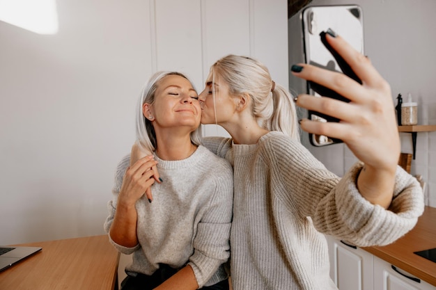 Loira jovem feliz mãe e filha na cozinha fazendo selfie para blog de família de blogs de redes sociais