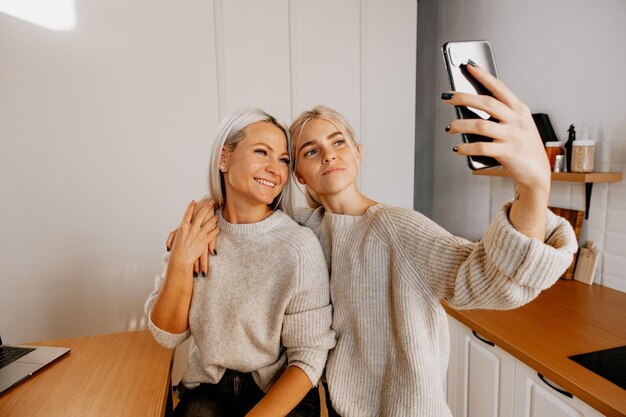 Loira jovem feliz mãe e filha na cozinha fazendo selfie para rede social e se divertindo muito blogando blog de família