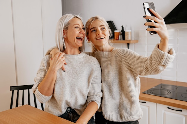 Loira jovem feliz mãe e filha na cozinha fazendo selfie para rede social e se divertindo muito blogando blog de família