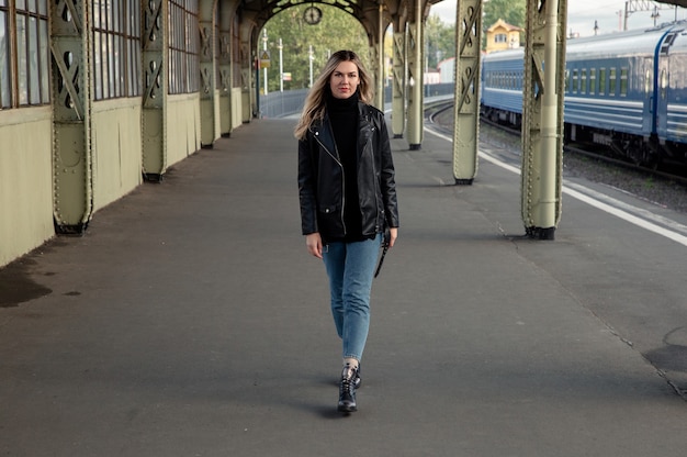 Loira linda com uma jaqueta de couro caminhando ao longo da plataforma da estação ferroviária