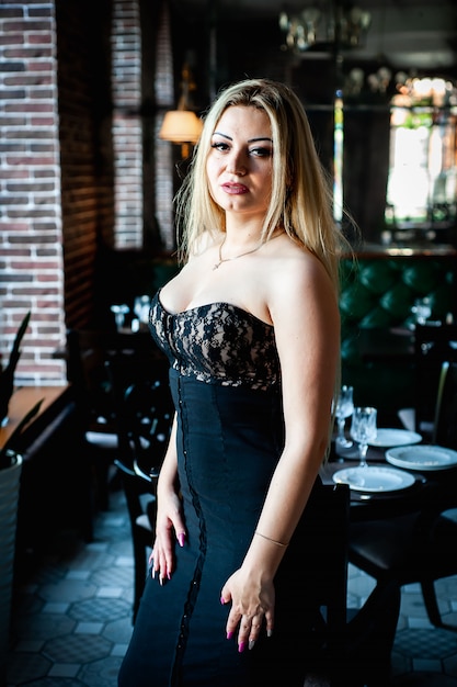 Loira linda de pé em um restaurante em um vestido preto e posando