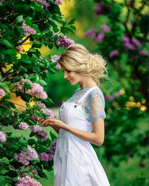 Loira linda em um vestido branco ao ar livre entre lilases