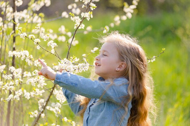Loira linda menina com cabelo comprido fareja um galho de árvore florida no parque na primavera.