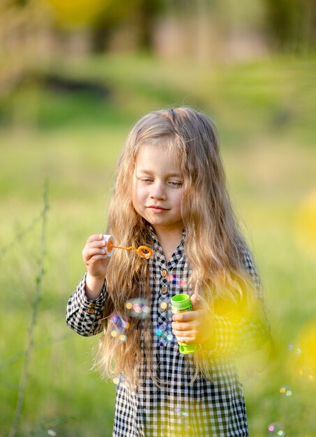 Loira menina bonitinha soprando bolhas de sabão, se divertindo no parque primavera.