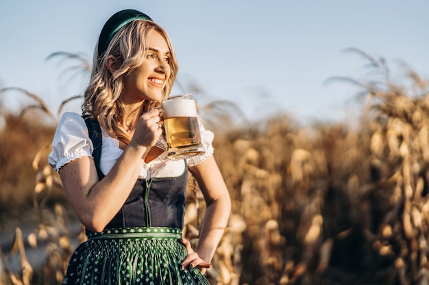 Foto loira muito feliz em vestidos casuais, tradicional festival, segurando a caneca de cerveja ao ar livre no campo