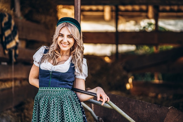 Loira muito sorridente no vestido tradicional com carrinho de mão trabalhando no quintal.