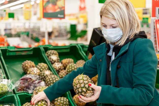 Loira mulher com uma máscara médica escolhe frutas em um supermercado. auto-isolamento em uma pandemia.