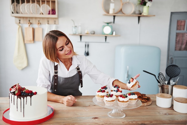 Loira positiva com seus deliciosos biscoitos caseiros e bolo na cozinha.