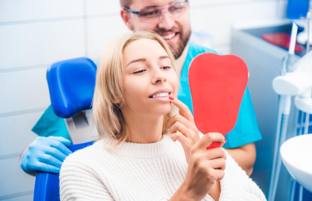 Loira satisfeita olhando no espelho vermelho depois do trabalho do dentista