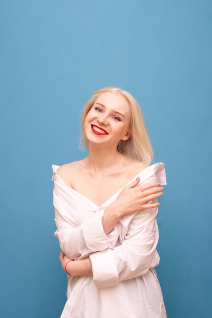 Loira sexy feliz em uma camisa de homem isolada em um fundo azul, olhando para a câmera