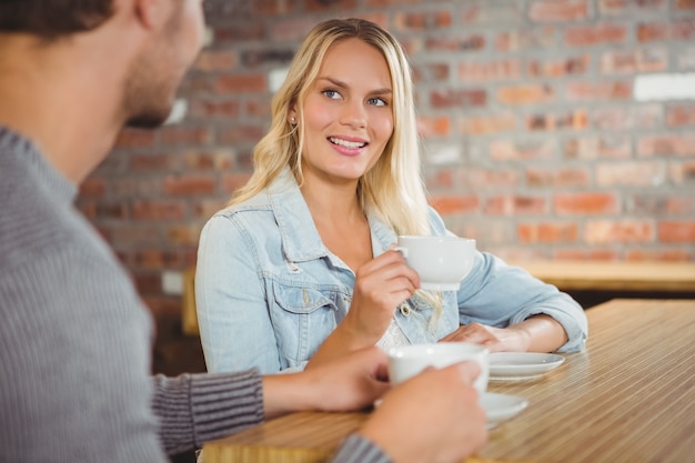 Loira sorridente tomando café com um amigo