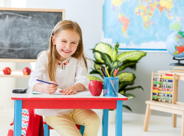 Loirinha, sentar à mesa branca escrevendo no caderno e rindo na turma da escola