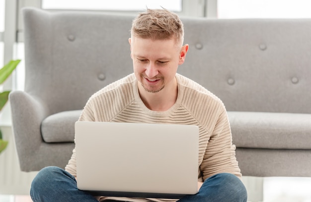 Loiro atraente sentado com um laptop, digitando e conversando usando a internet