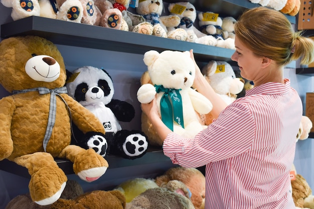 Loja de brinquedos de pelúcia. O comprador escolhe o brinquedo. Uma mulher compra um ursinho de pelúcia. presente para criança