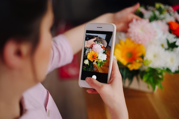 Loja de flores uma florista fotografa uma composição de flores em um smartphone para redes sociais
