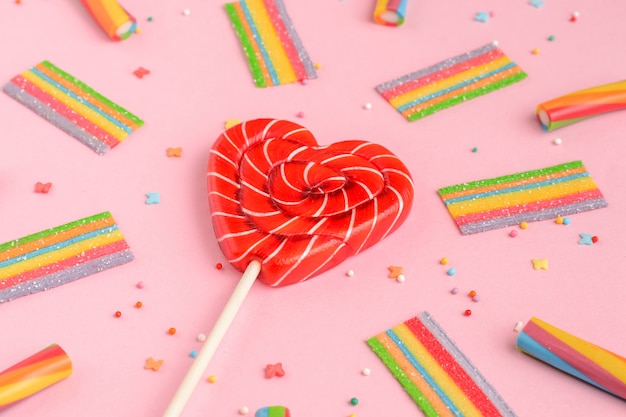 Lollipop rojo en forma de corazón y dulces de colores sobre un fondo rosa