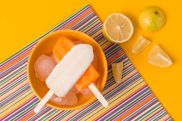 Lolly de gelo brilhante na tigela perto de guardanapo e frutas frescas