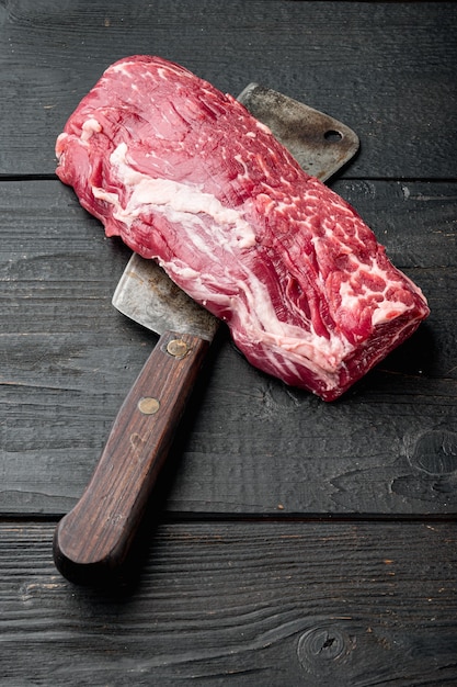Foto lombo, ou filé de olho, cortado em conjunto de carne bovina de mármore crua, com uma velha faca de cutelo de açougueiro, sobre fundo preto de mesa de madeira