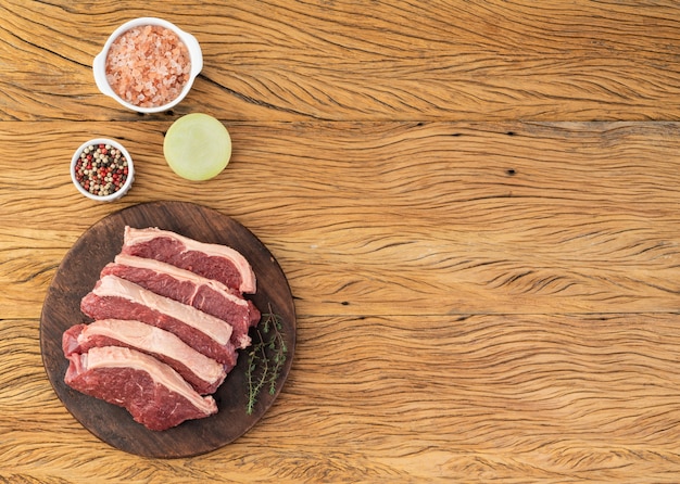 Lomo de carne cruda en rodajas sobre tabla de madera con condimentos y copie el espacio.