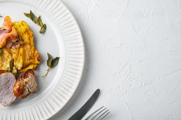 Lomo de cerdo al horno con patatas y hierbas, en plato plato, sobre piedra blanca