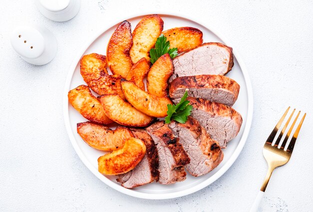 Lomo de cerdo al horno con rodajas de membrillo o manzana servido en un plato Vista superior del fondo de la mesa blanca