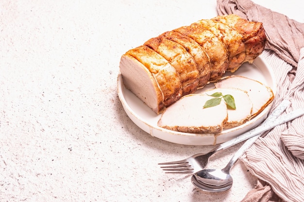 Lomo de cerdo al horno sobre un soporte de cerámica con cubiertos. Una moderna luz dura, sombra oscura, fondo de masilla blanca, lugar para texto