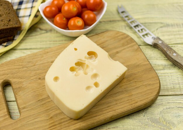 Una loncha de queso sobre una tabla para cortar y tomates cherry junto a una superficie de madera