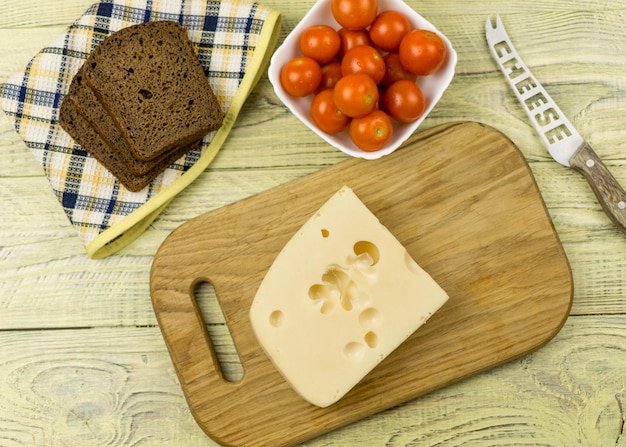 Una loncha de queso sobre una tabla para cortar y tomates cherry junto a una superficie de madera