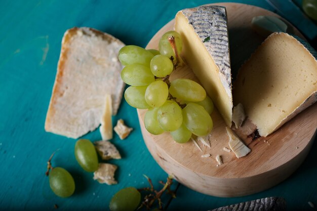 Lonchas de queso, uvas blancas, cuchillo, vaso y una botella de vino blanco sobre una superficie de madera. De cerca