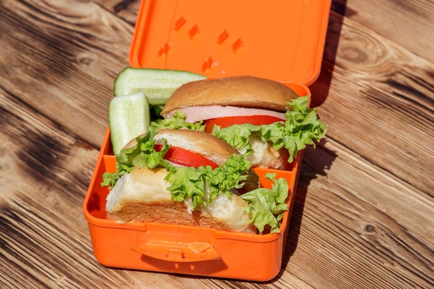 Lonchera escolar con dos hamburguesas caseras y pepinos frescos en una mesa de madera