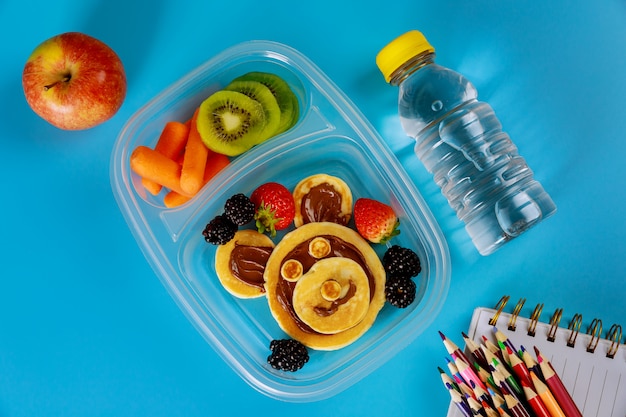 Lonchera escolar con panqueques, frutas frescas y una botella de agua.
