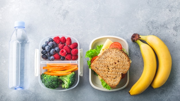 Lonchera escolar con sándwich de verduras bayas de plátano en la mesa gris saludable