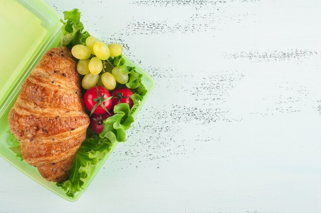 Lonchera verde con croissant, ensalada