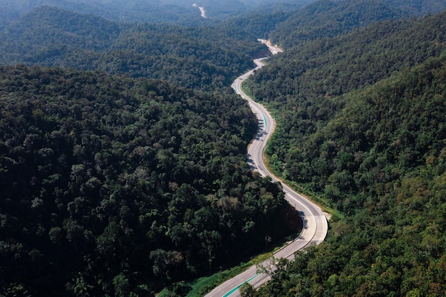 Longa estrada curvada no vale conectando o campo na floresta tropical e a floresta verdejante na parte norte da Tailândia, vista aérea de um tiro de drone