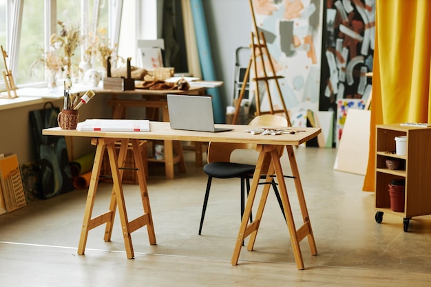 Longa mesa de madeira com pincéis de tela para laptop e tubos com tintas no centro de sp
