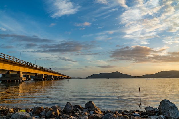 Longa ponte de concreto atravessando o lago com céu azul e montanha