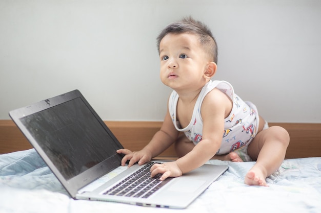 La longitud completa del bebé jugando con la computadora portátil en casa