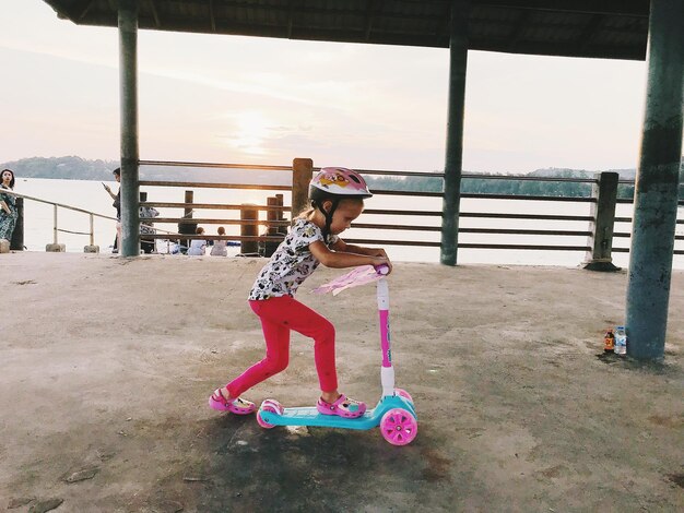 Foto la longitud completa de una chica linda montando un scooter de empuje en la pasarela