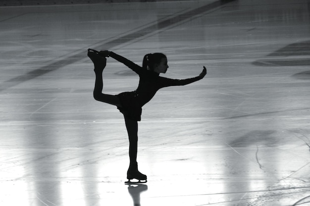 La longitud completa de la chica patinando en el hielo en la pista de patinaje