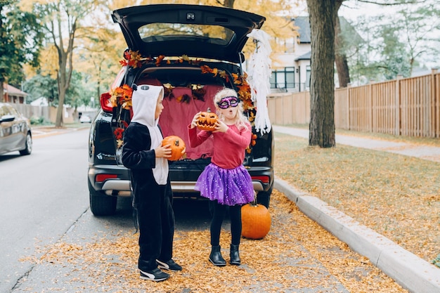 longitud completa de hermano lindo sosteniendo calabaza de pie junto al coche