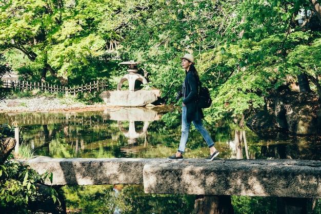 longitud completa del hombre de la lente de la chica joven que disfruta caminando en la hermosa e increíble nihon teien. alegre viajero caminando sobre un puente de piedra a través del estanque con agua limpia. Visita el jardín japonés tradicional.