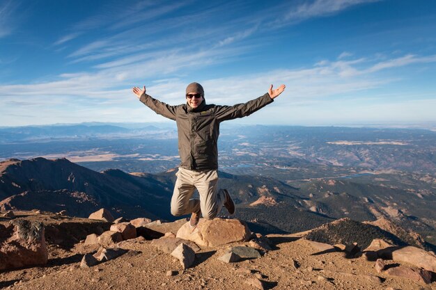 La longitud completa del hombre saltando en el aire y disfrutando de estar en la parte superior de las picas pico de Colorado contra el cielo