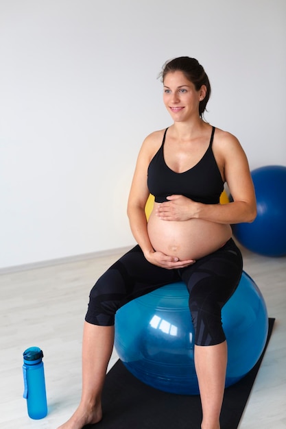 Foto la longitud completa de una joven embarazada tocando el abdomen mientras está sentada en una pelota de fitness