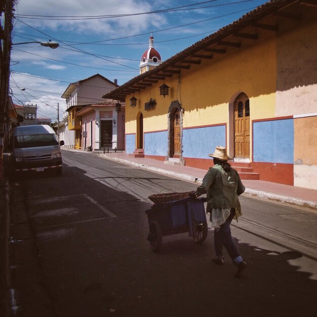 Foto la longitud completa de la mujer empujando la carretilla en la calle por las casas