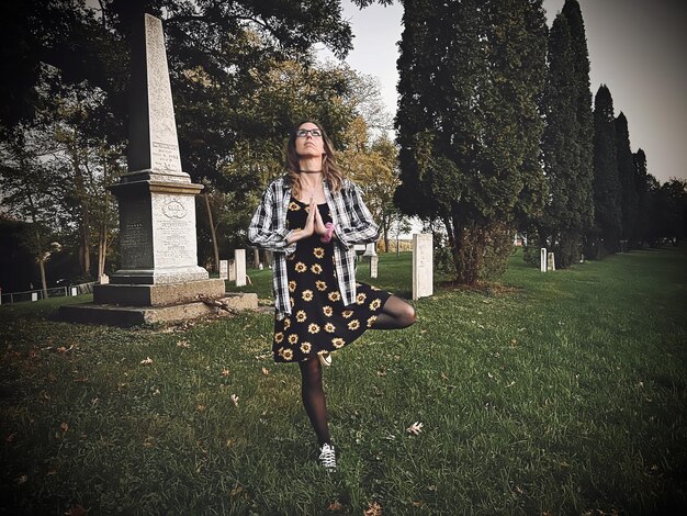 La longitud completa de una mujer joven en el cementerio haciendo la postura del árbol de yoga