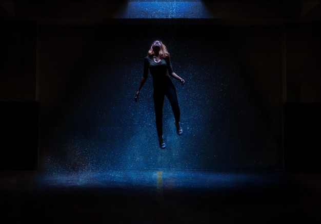 longitud completa de una mujer joven levitando en el cuarto oscuro