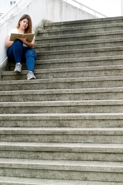 Foto longitud completa de una mujer joven leyendo un libro mientras está sentada en los escalones