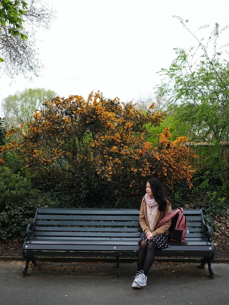 Foto la longitud completa de la mujer sentada en un banco en el parque