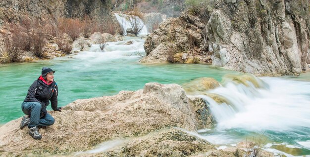 La longitud completa de la mujer sentada en las rocas en la cascada